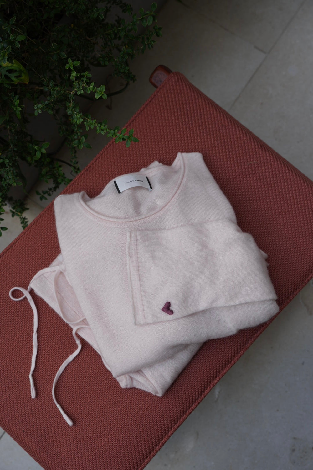 A pale blush pink long-sleeve crewneck knit top, shown flat against a solid taupe-gray background.