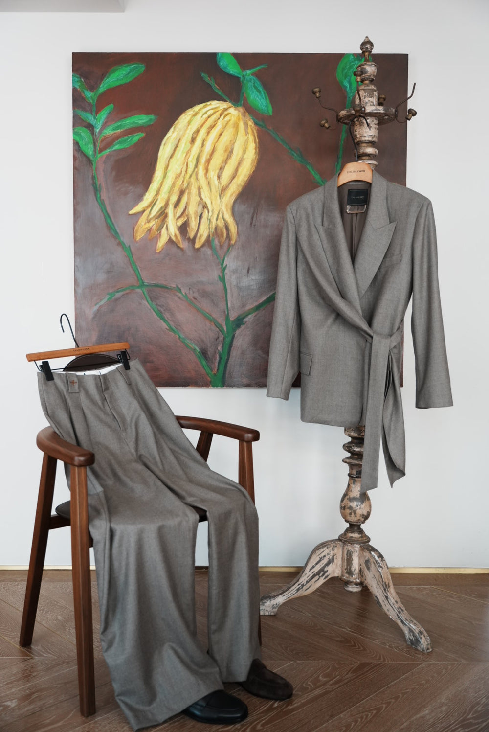 A gray wrap-style blazer with a self-tie belt, shown against a solid taupe background.