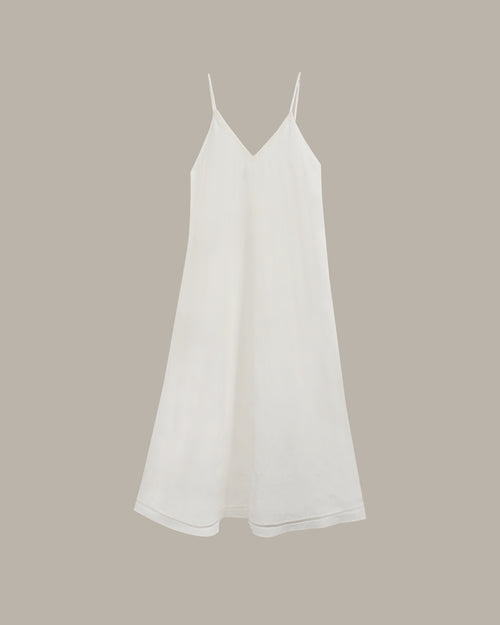 A white sleeveless slip dress with thin spaghetti straps and a V-neckline, shown against a solid taupe background.
