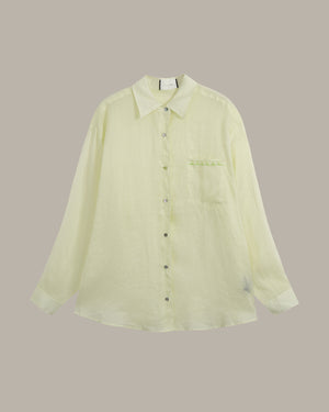 A pale yellow-green long-sleeve button-up shirt with a pointed collar, dark buttons, and a chest pocket, displayed against a solid taupe background.