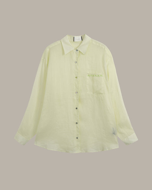 A pale yellow-green long-sleeve button-up shirt with a pointed collar, dark buttons, and a chest pocket, displayed against a solid taupe background.