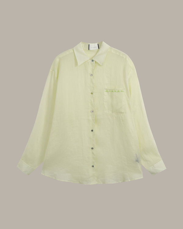 A pale yellow-green long-sleeve button-up shirt with a pointed collar, dark buttons, and a chest pocket, displayed against a solid taupe background.