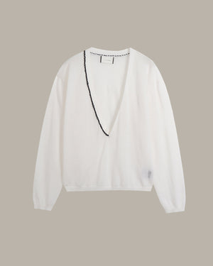 A white long-sleeve knit top with a deep V-neckline, featuring a black beaded trim detail running down the front center, displayed against a solid taupe background.