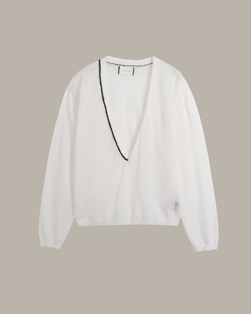 A white long-sleeve knit top with a deep V-neckline, featuring a black beaded trim detail running down the front center, displayed against a solid taupe background.