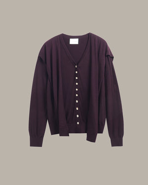 A dark plum purple cardigan sweater with a V-neck, front button closure, and unique draped shoulder detailing, shown against a solid taupe background.