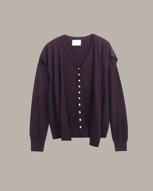 A dark plum purple cardigan sweater with a V-neck, front button closure, and unique draped shoulder detailing, shown against a solid taupe background.