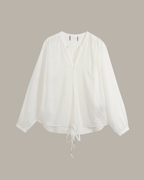 A white long-sleeve blouse with a split V-neckline and a drawstring tie at the hem, displayed against a solid taupe background.
