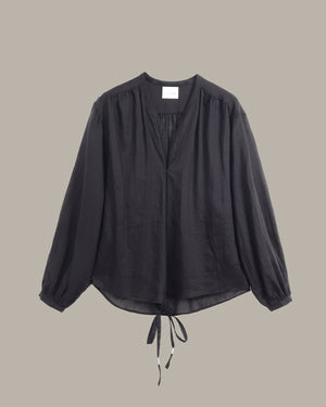 A black long-sleeve blouse with a split V-neckline, gathered shoulders, and a drawstring tie at the hem, displayed against a solid taupe background.