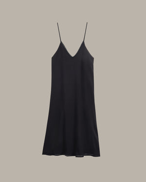 A black satin slip dress with thin spaghetti straps and a V-neckline, displayed against a solid taupe-gray background.