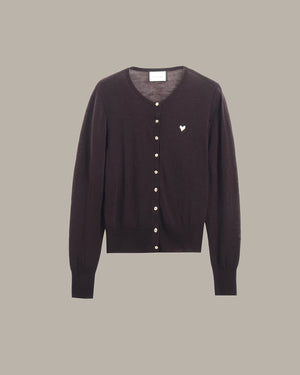 A dark brown button-up cardigan sweater with a small white embroidered heart on the left chest, displayed against a solid taupe background.