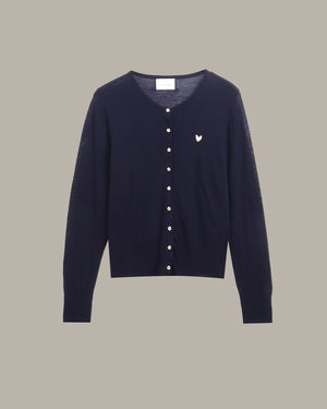 A navy blue knit cardigan sweater with a small white embroidered bird logo on the left chest, displayed against a solid taupe background.