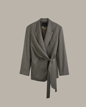 A gray wrap-style blazer with a self-tie belt, shown against a solid taupe background.