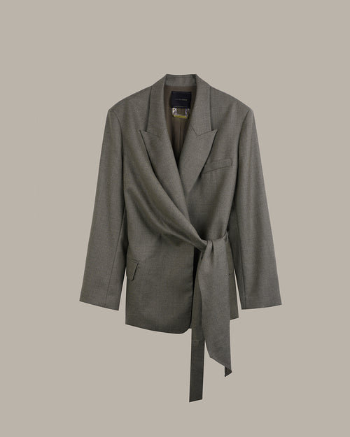 A gray wrap-style blazer with a self-tie belt, shown against a solid taupe background.