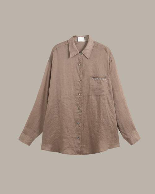 A taupe-brown long-sleeve button-up shirt with a pointed collar and a chest pocket featuring decorative silver studs, shown against a solid taupe background.