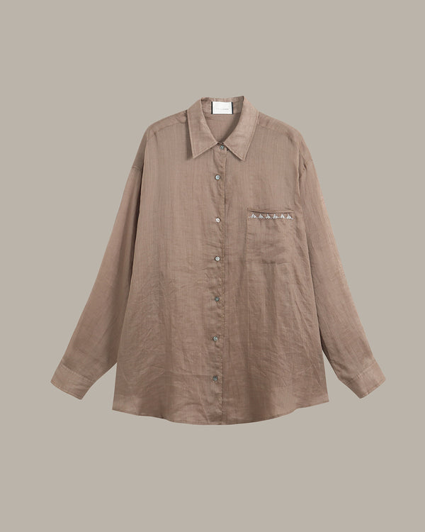 A taupe-brown long-sleeve button-up shirt with a pointed collar and a chest pocket featuring decorative silver studs, shown against a solid taupe background.