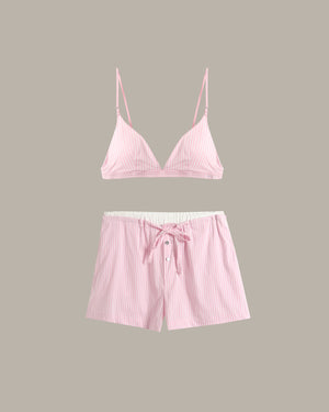 A two-piece pink lounge set featuring a thin-strap triangle top and matching drawstring shorts with a white inner lining, displayed against a solid taupe background.