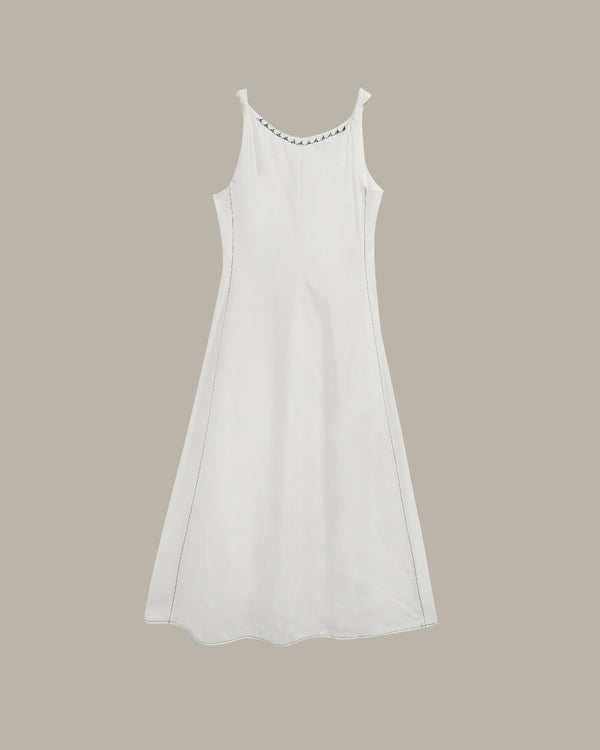 A white sleeveless slip dress with a scoop neckline accented by a row of small dark rhinestones, shown against a solid taupe background.