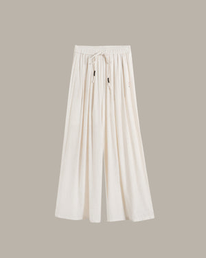 A pair of off-white wide-leg pants with an elastic drawstring waist, displayed against a solid taupe background.