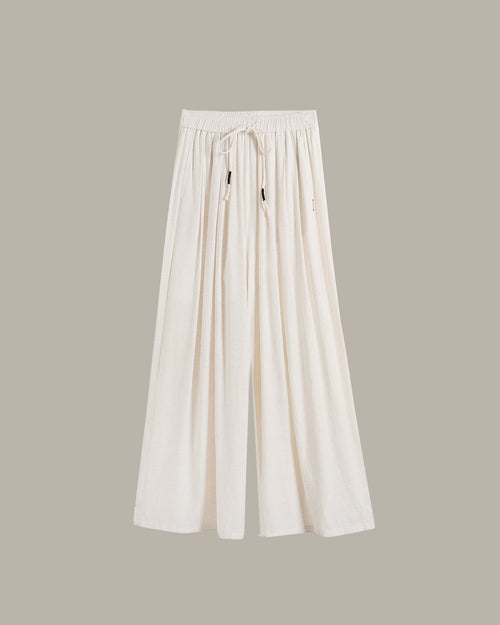 A pair of off-white wide-leg pants with an elastic drawstring waist, displayed against a solid taupe background.
