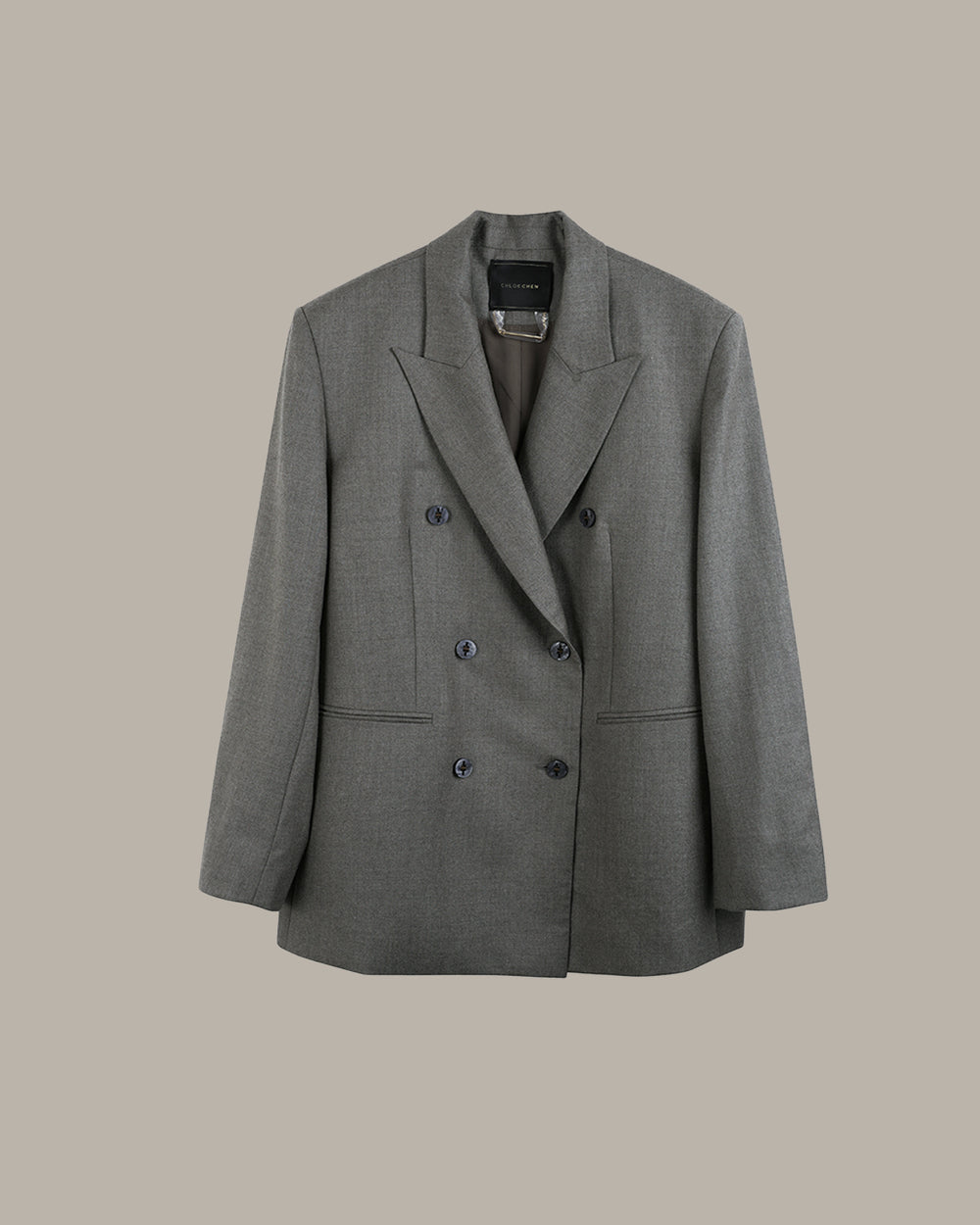 A gray double-breasted blazer with notched lapels and dark buttons, displayed against a solid beige background.