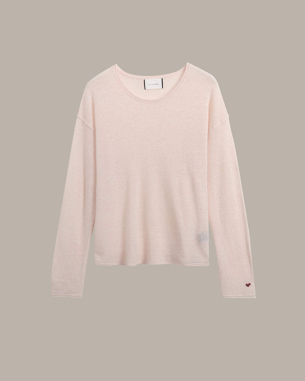 A pale blush pink long-sleeve crewneck knit top, shown flat against a solid taupe-gray background.
