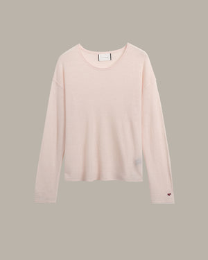 A pale blush pink long-sleeve crewneck knit top, shown flat against a solid taupe-gray background.