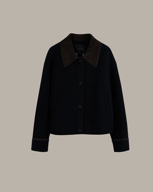A dark navy blue cropped jacket with a contrasting dark brown suede collar and matching brown button details, displayed against a solid taupe background.