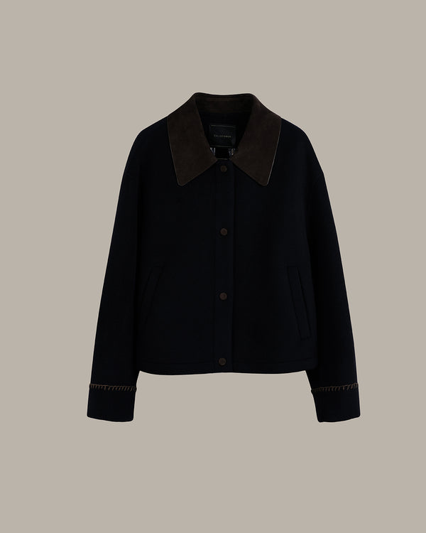 A dark navy blue cropped jacket with a contrasting dark brown suede collar and matching brown button details, displayed against a solid taupe background.
