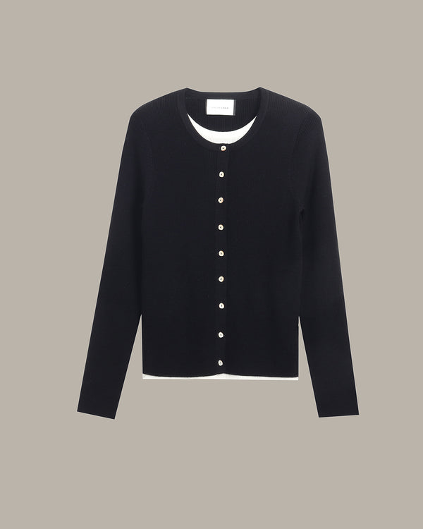 A black long-sleeve cardigan sweater with a white inner collar and a vertical row of white buttons down the front, displayed against a solid taupe background.