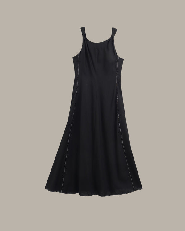 A black sleeveless A-line dress with thin shoulder straps and subtle contrast stitching, shown against a solid taupe background.