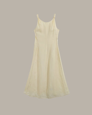 A light yellow-colored sleeveless slip dress with thin spaghetti straps, shown against a solid taupe-gray background.