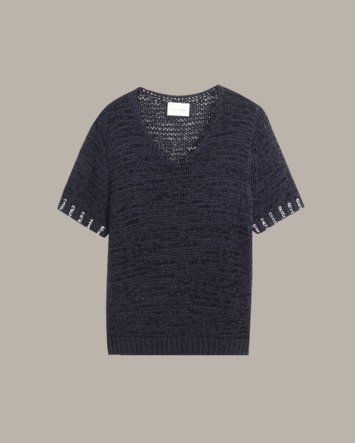 A dark navy blue knit short-sleeve top with a V-neck and decorative white embroidered lettering along the sleeve cuffs, displayed flat against a solid taupe background.