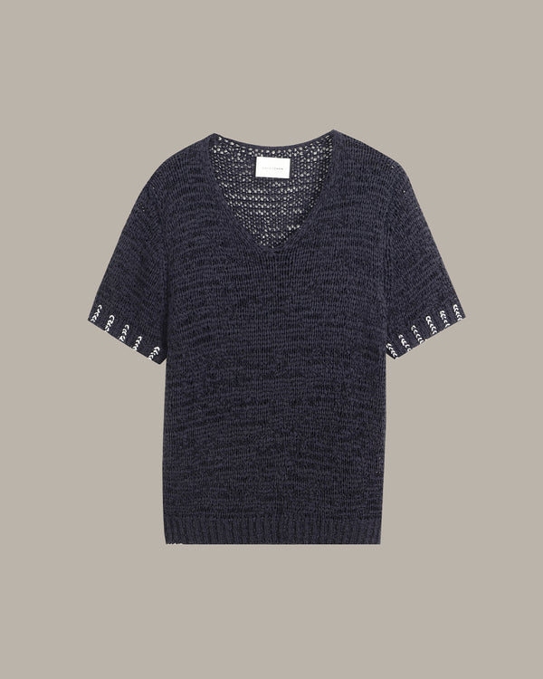 A dark navy blue knit short-sleeve top with a V-neck and decorative white embroidered lettering along the sleeve cuffs, displayed flat against a solid taupe background.