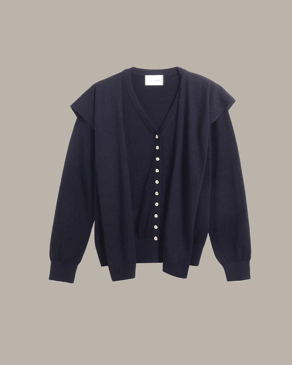 A dark navy blue cardigan sweater with a V-neck, button-front closure, and wide shoulder panels, shown against a solid taupe background.