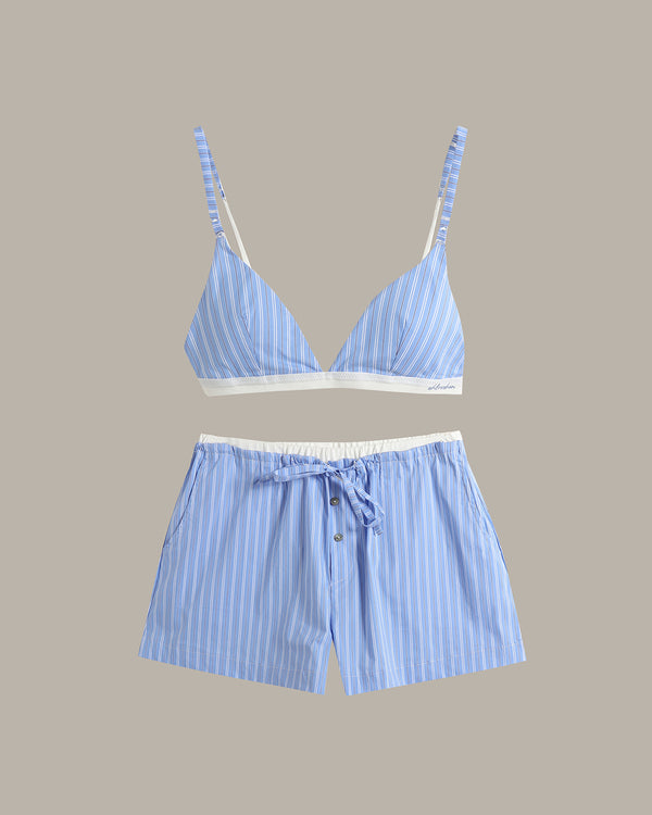 A two-piece loungewear set featuring a light blue and white striped triangle bikini top with white trim and matching striped shorts with a white drawstring waist, displayed on a solid taupe background.