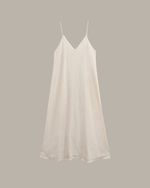 A light cream-colored slip dress with thin spaghetti straps and a V-neckline, displayed against a solid taupe-gray background.