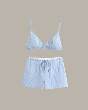A two-piece loungewear set featuring a light blue and white striped triangle bralette with thin straps and matching drawstring shorts with a white buttoned placket, displayed on a solid beige background.