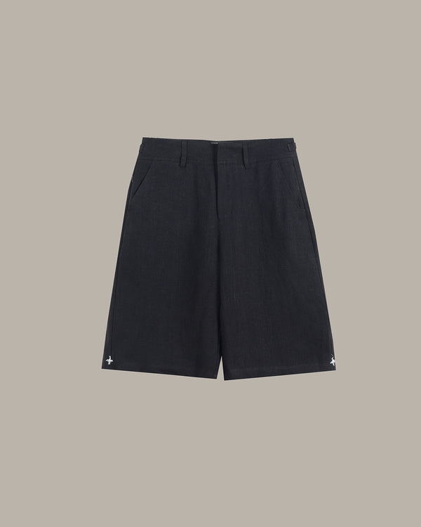 A pair of dark charcoal gray shorts with a subtle textured weave, featuring small white embroidered star details on the lower hems, displayed against a solid taupe background.
