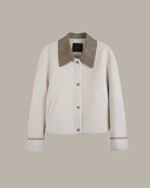 An off-white cropped jacket with a contrasting taupe suede-like collar, button-front closure, and decorative cuff detailing, shown against a solid taupe background.