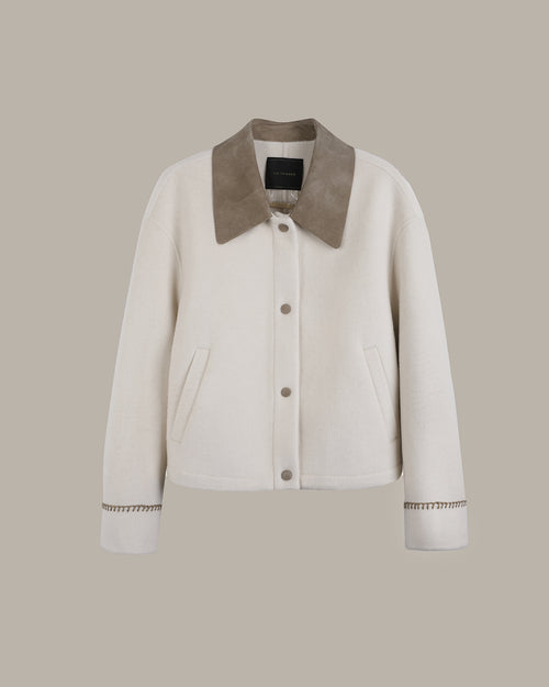 An off-white cropped jacket with a contrasting taupe suede-like collar, button-front closure, and decorative cuff detailing, shown against a solid taupe background.