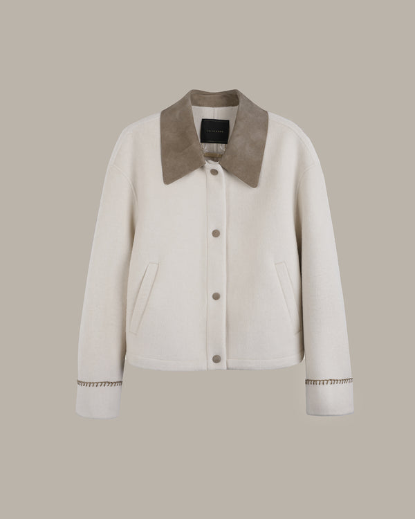 An off-white cropped jacket with a contrasting taupe suede-like collar, button-front closure, and decorative cuff detailing, shown against a solid taupe background.