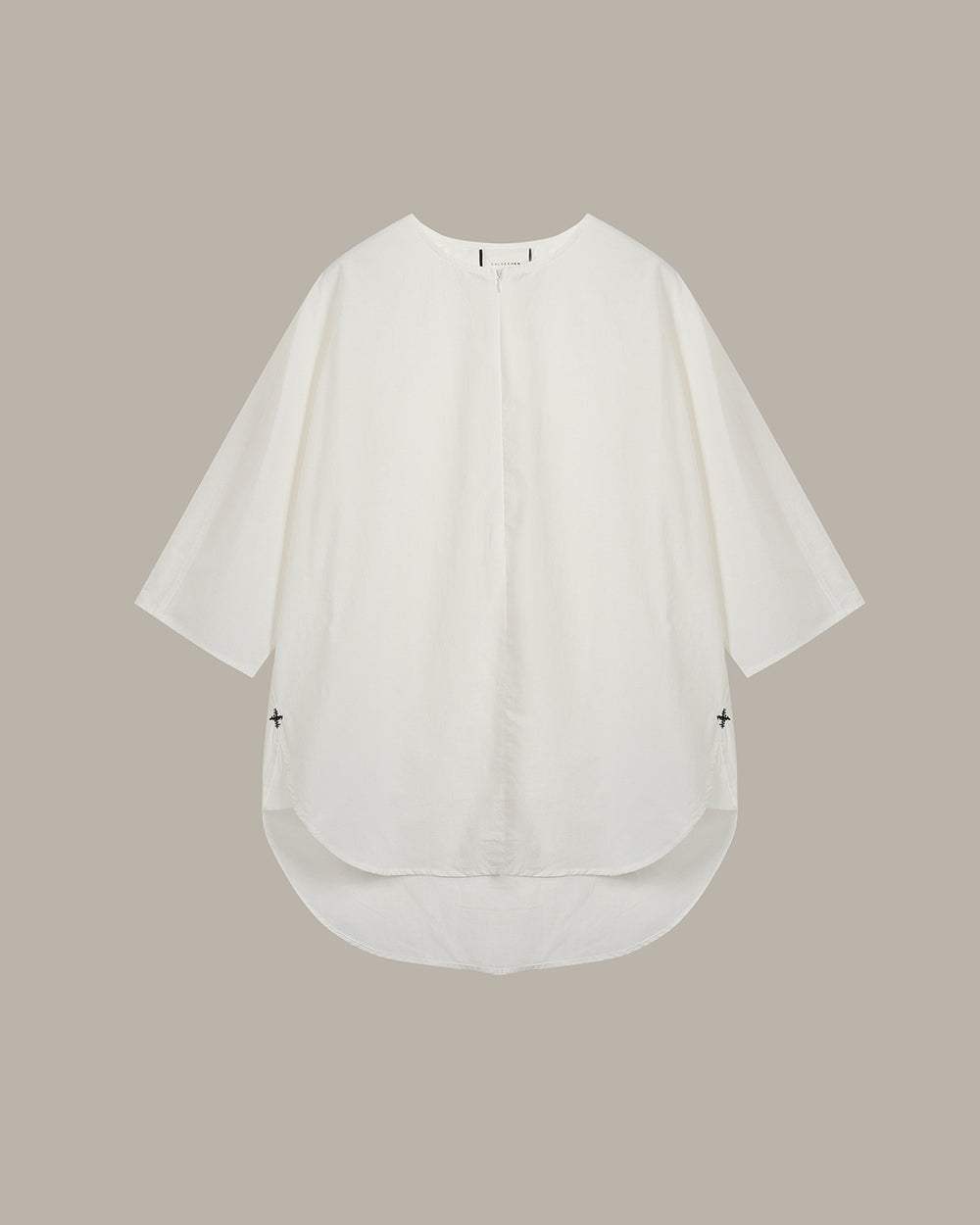 An  white, loose-fitting short-sleeve top with a high-low hem and small black embroidered crosses on the sides, displayed flat against a solid taupe background.
