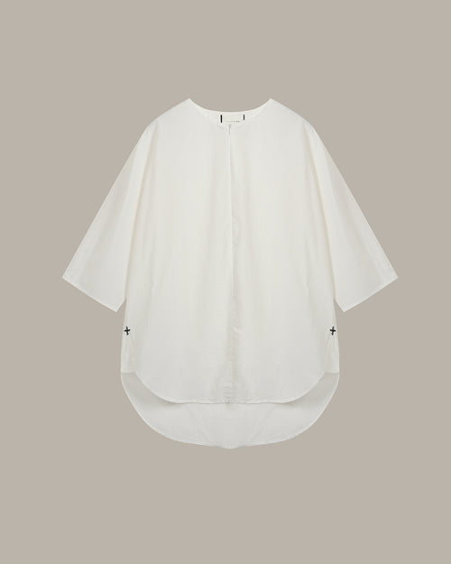 An  white, loose-fitting short-sleeve top with a high-low hem and small black embroidered crosses on the sides, displayed flat against a solid taupe background.