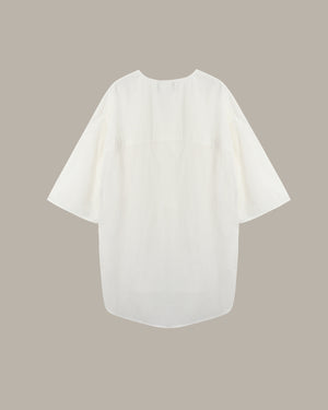 An off-white short-sleeve blouse with a relaxed, oversized fit, displayed flat against a solid taupe background.