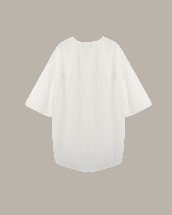 An off-white short-sleeve blouse with a relaxed, oversized fit, displayed flat against a solid taupe background.
