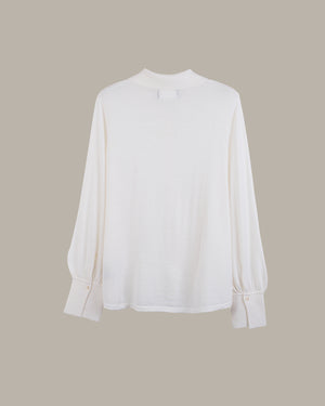 A white long-sleeve blouse with a mock neck and gathered cuffs, displayed against a solid taupe background.
