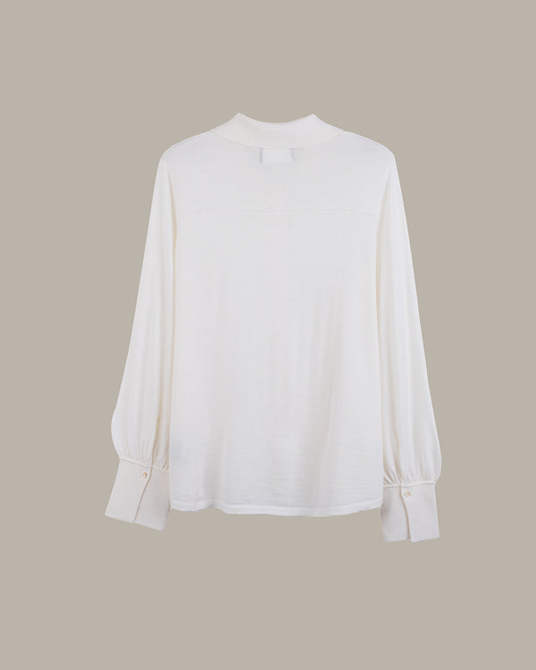 A white long-sleeve blouse with a mock neck and gathered cuffs, displayed against a solid taupe background.
