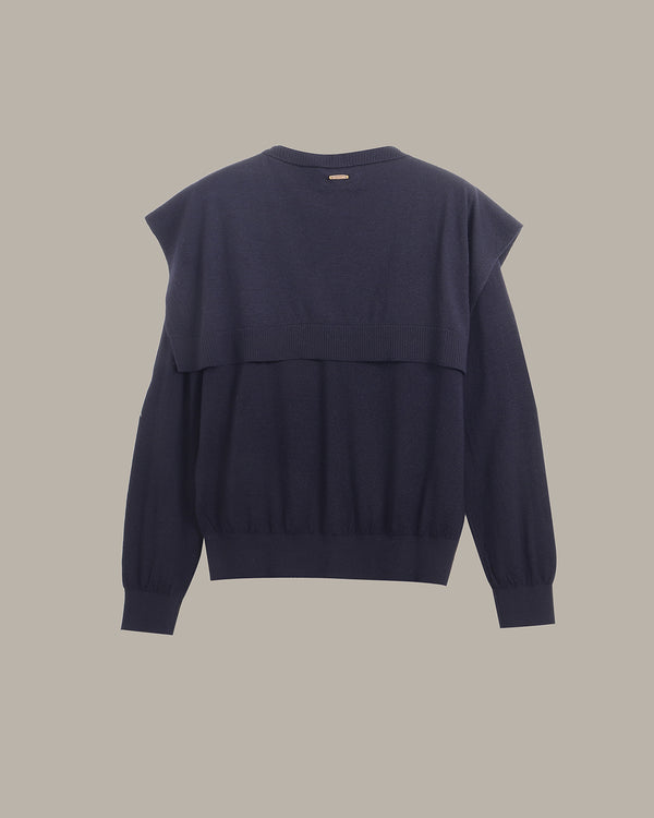 A dark navy blue knit sweater with a unique layered, asymmetrical shoulder design, shown from the back against a solid neutral beige background.