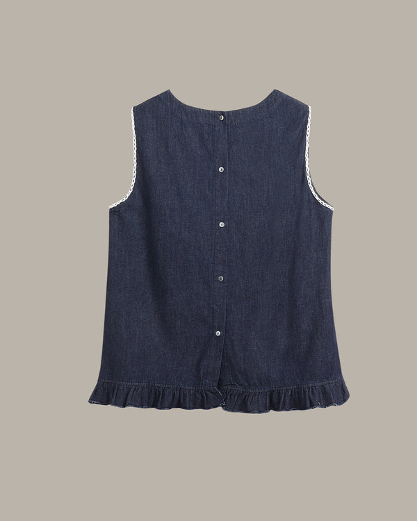 A sleeveless dark blue denim-style top with a ruffled hem, button front, and white lace trim along the armholes, shown on a plain taupe background.