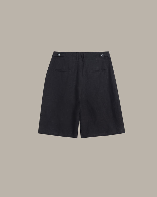 Black wide-leg shorts with a buttoned waistband and flap pockets, shown flat against a solid taupe background.